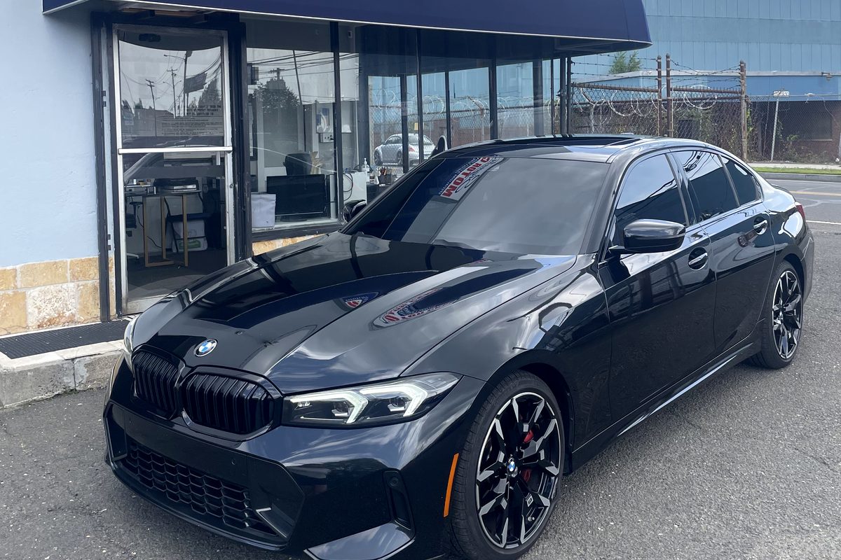 2025 BMW 330i M Sport in black, parked outside the Signature Motor Cars showroom
